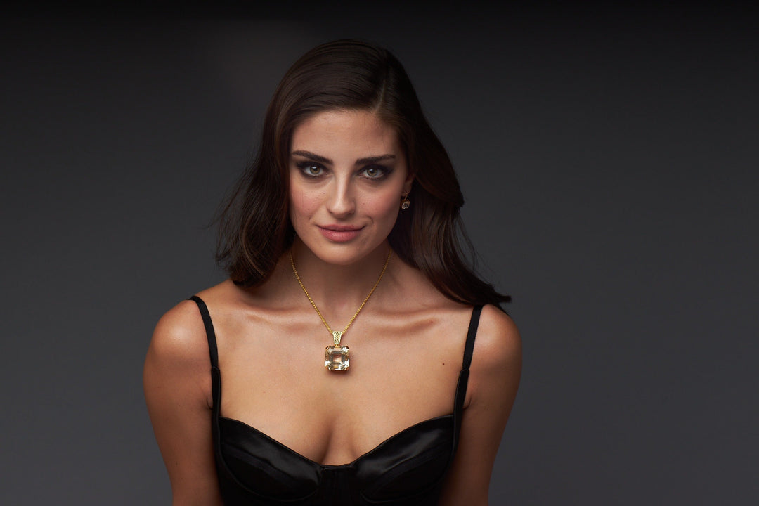 A woman wearing a gold necklace with lighting that evokes iridescent moissanite stones in a raw mineral cluster showing shifting colours, similar to natural diamonds and diamond simulant gems across different carat weight in moissanite rings.