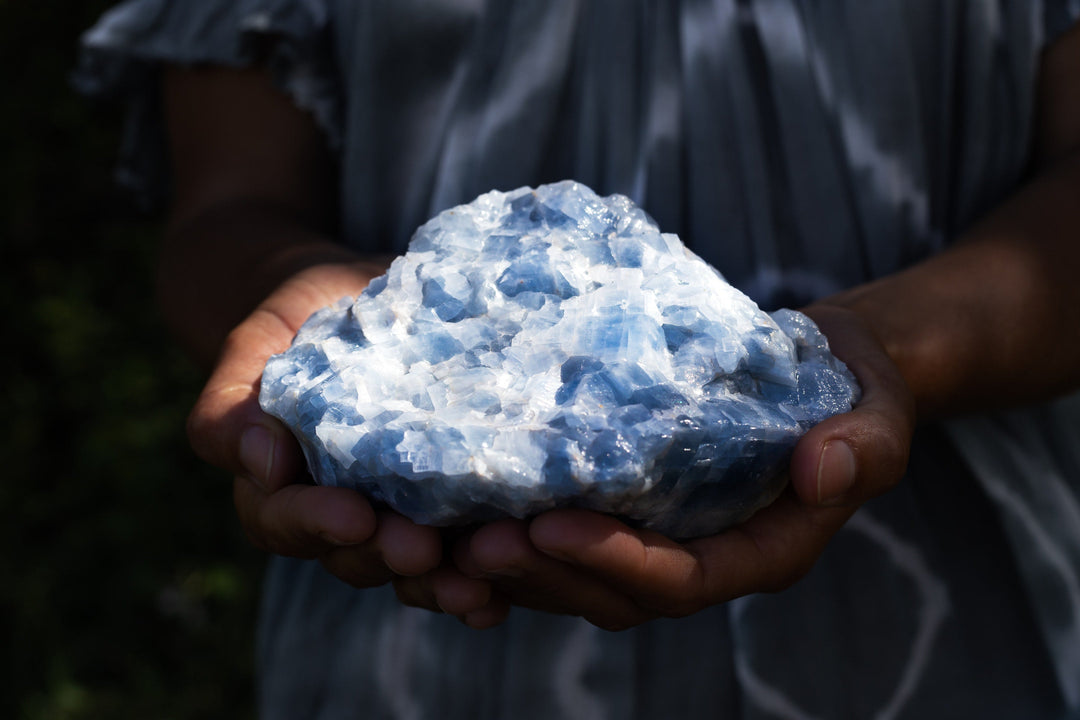 Hands holding a large raw blue crystal radiating light codes for spiritual healing, emotional healing, crystal healing, personal growth, and higher consciousness.