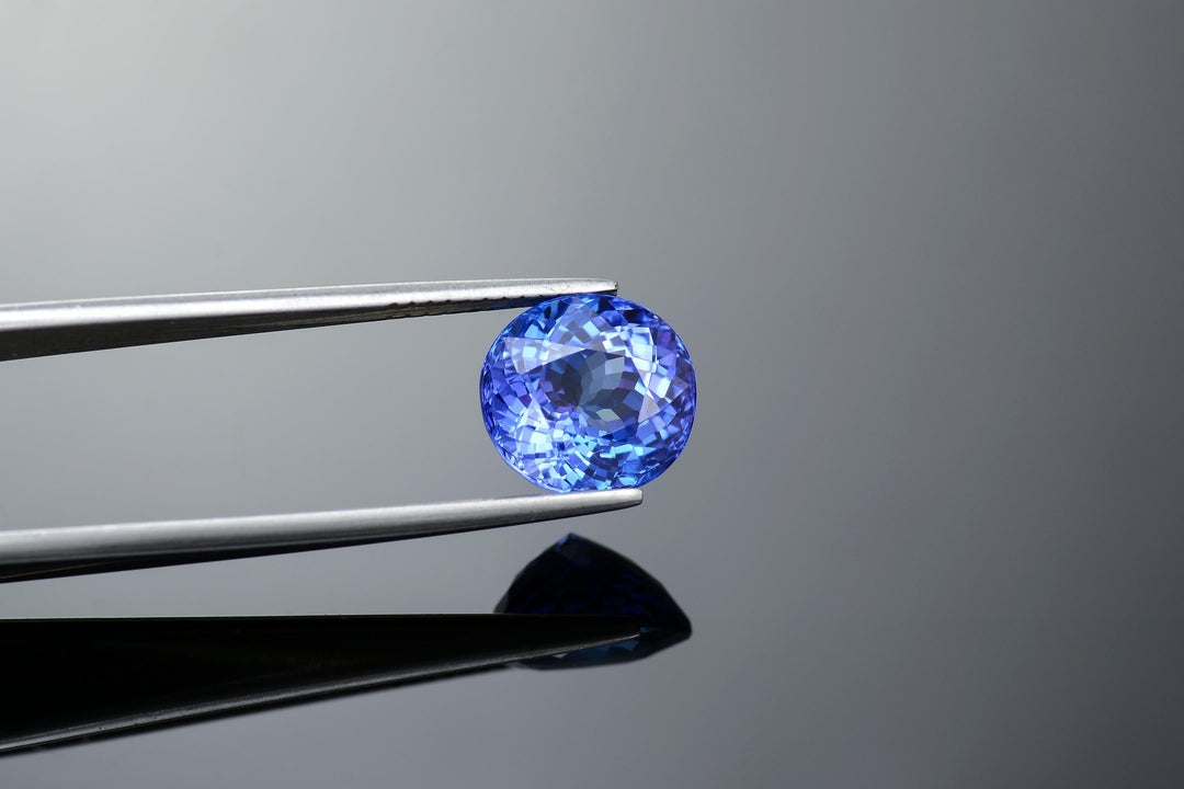 tanzanite gemstone in a blue color violet oval cut stone held in tweezers